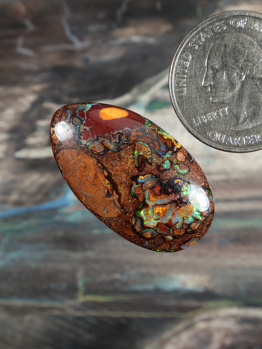 Oval boulder opal cabochon, warm orange base with bright blue-green flash