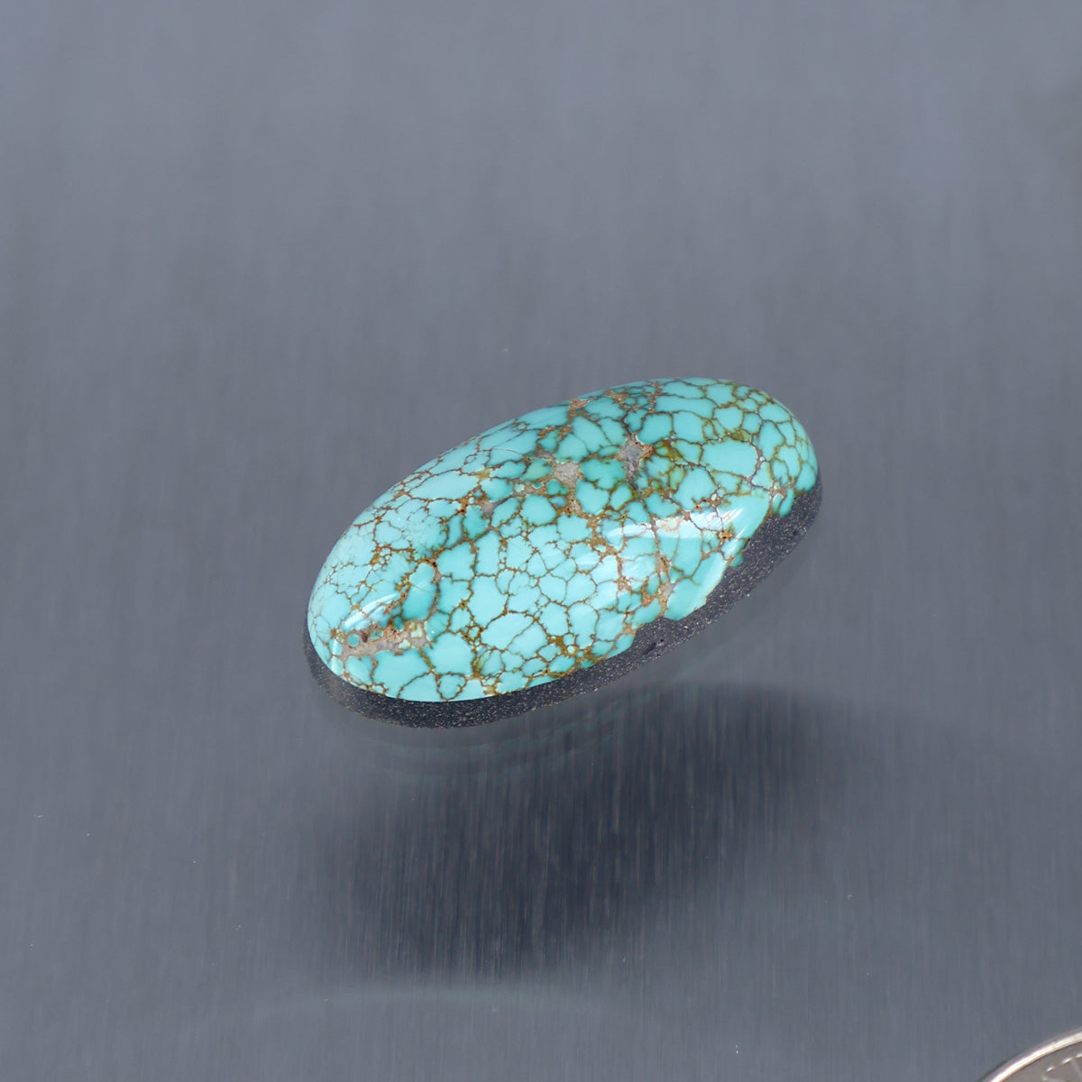 Turquoise oval cabochon with intricate gold web pattern, smooth polished surface.