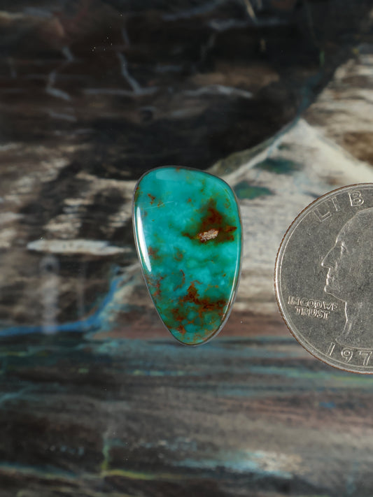 Turquoise teardrop cabochon gemstone with red-brown matrix veining, polished.