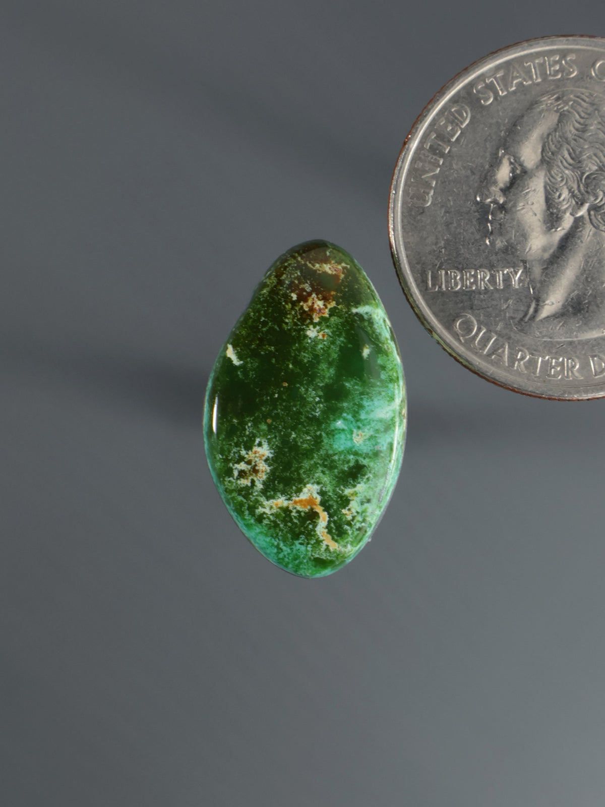 Green oval cabochon gemstone with mottled speckled surface
