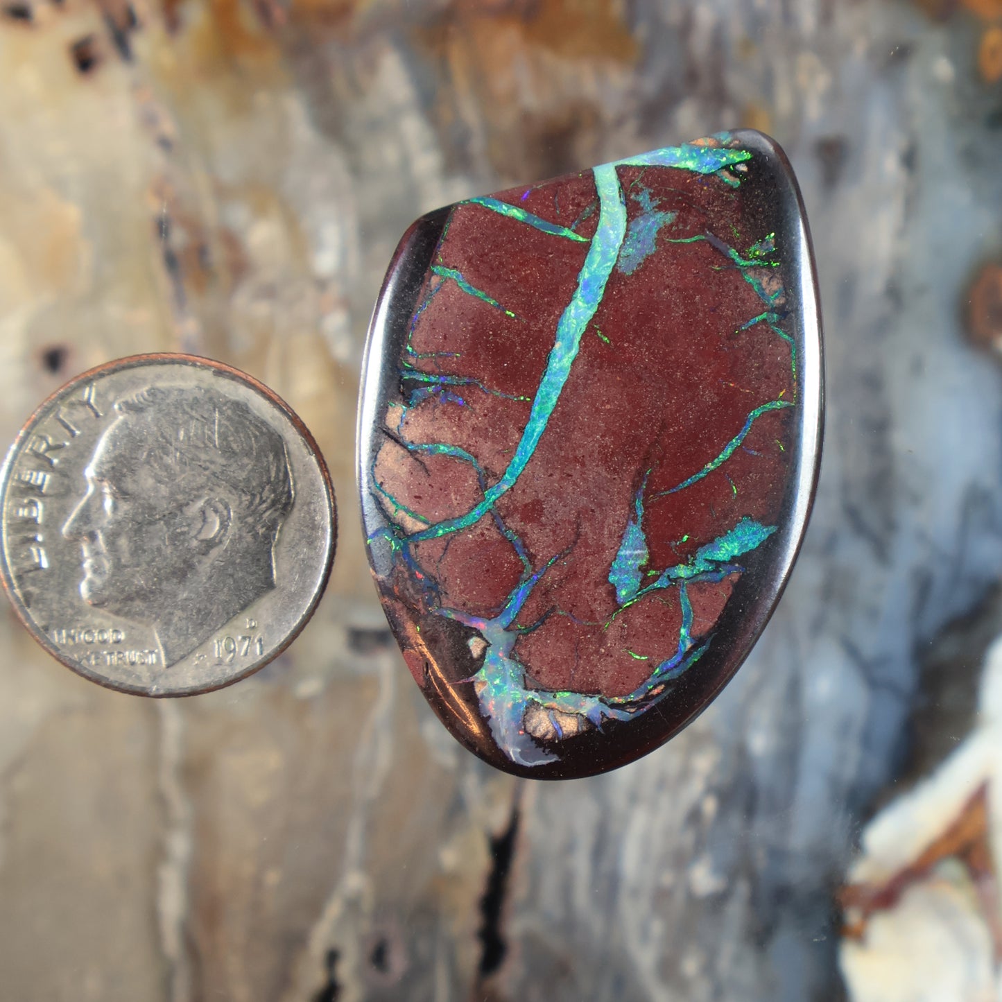 Oval boulder opal cabochon with deep red body and bright teal-blue vein pattern, polished