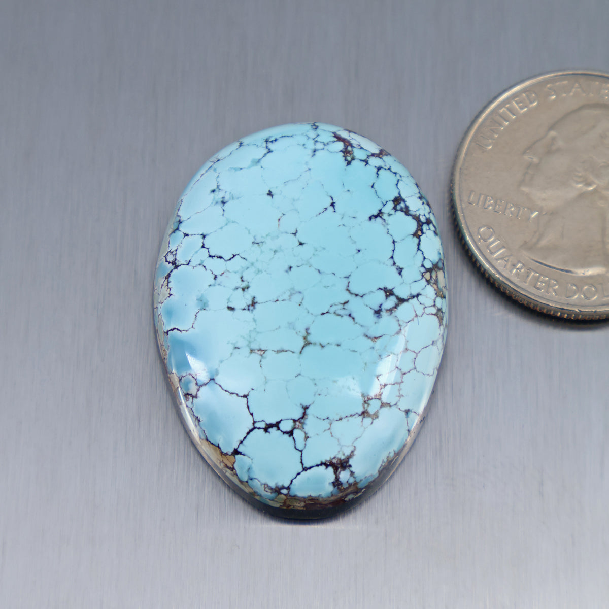 Blue turquoise oval cabochon with dark matrix veining and metal bezel