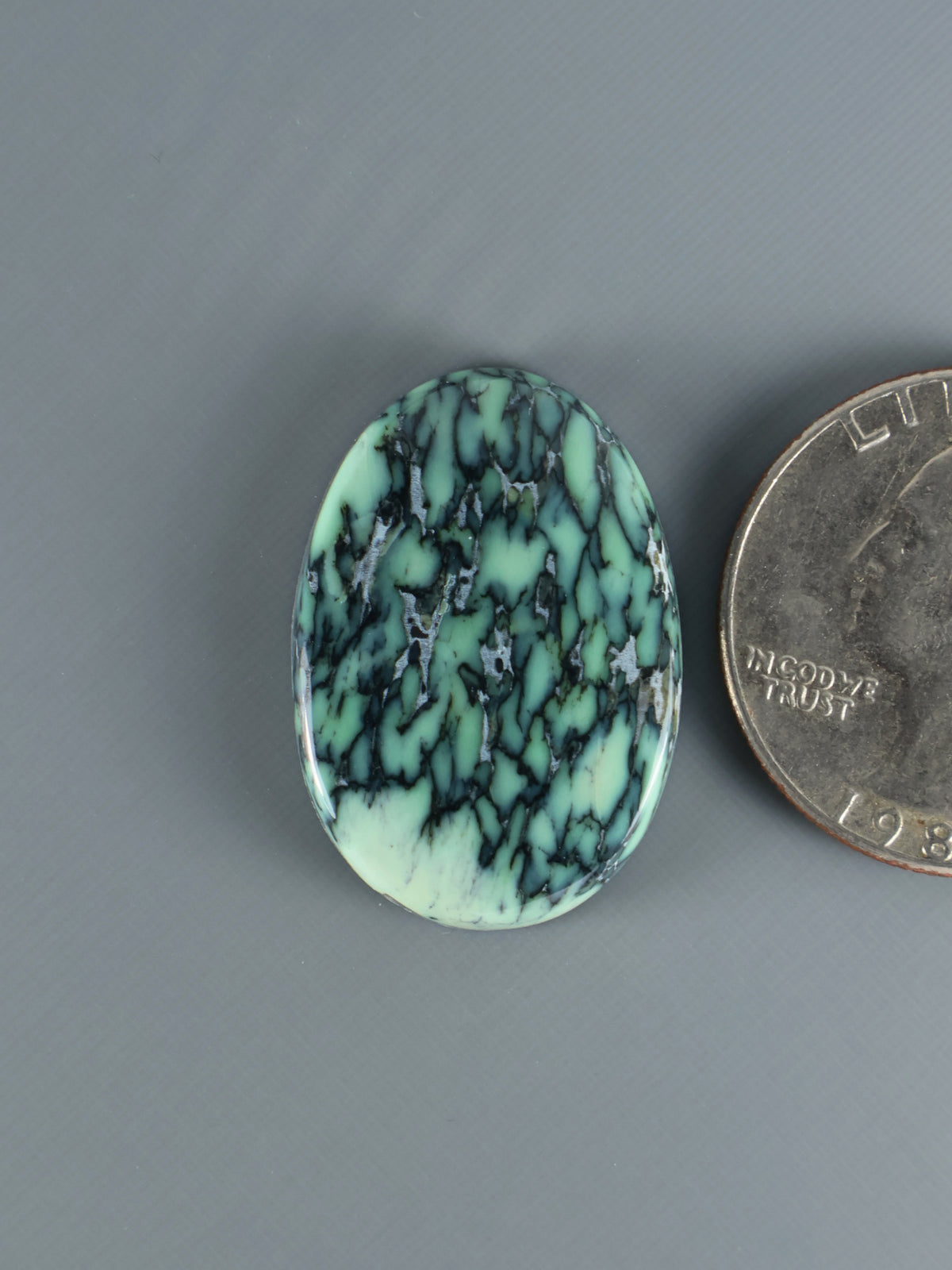 Oval variscite cabochon with turquoise-green color and dark matrix veining