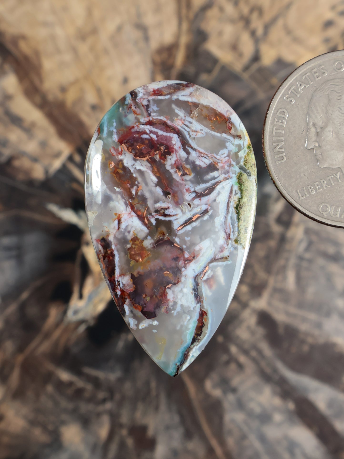 Oval teardrop cabochon gemstone with pale aqua/blue areas and copper-brown red speckling