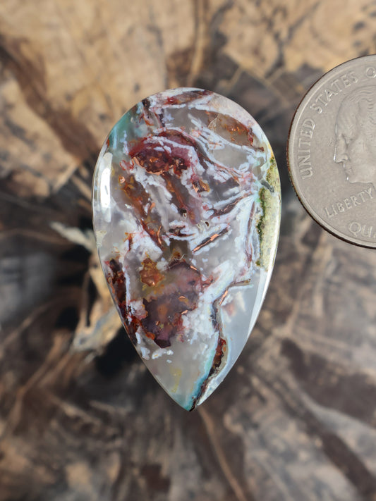 Oval teardrop cabochon gemstone with pale aqua/blue areas and copper-brown red speckling