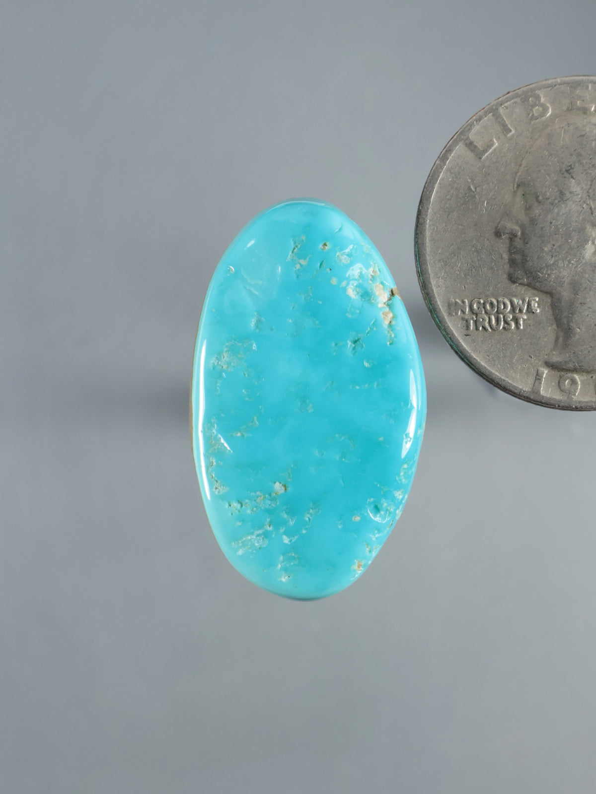 Oval Sleeping Beauty turquoise cabochon with natural matrix, shown beside a coin for scale