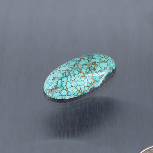 Turquoise oval cabochon with intricate gold web pattern, smooth polished surface.