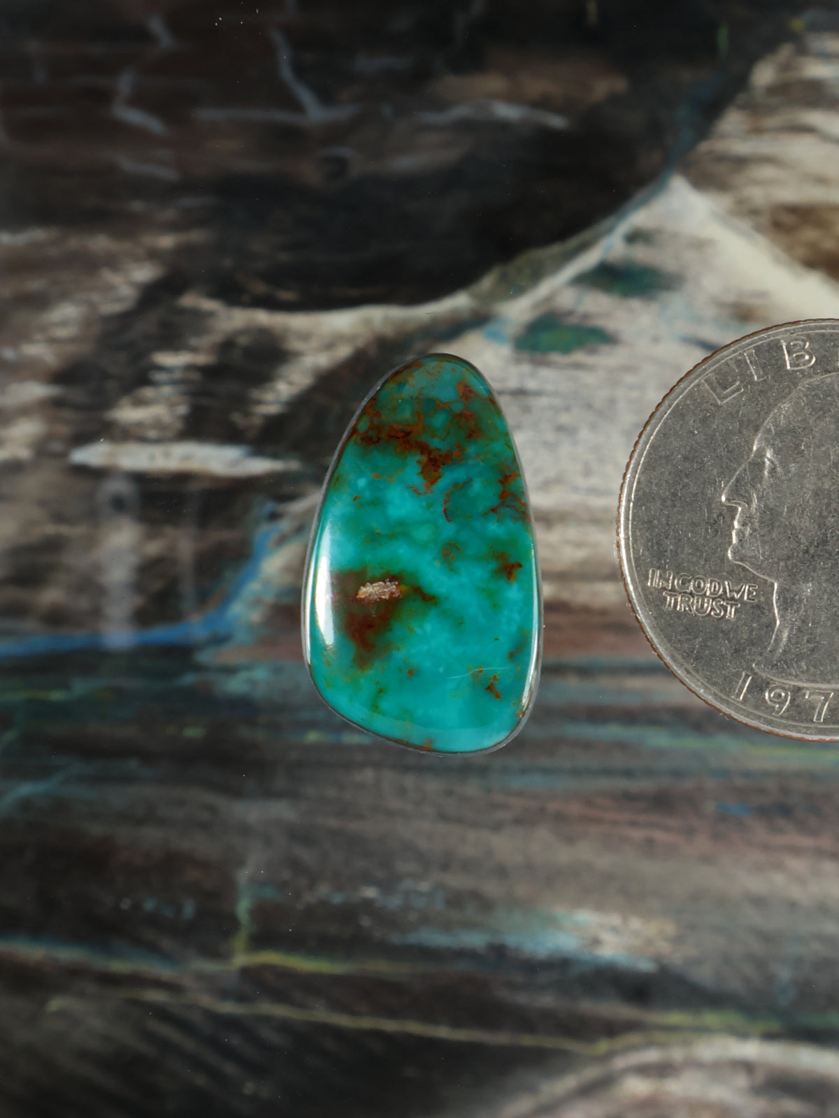 Turquoise teardrop cabochon gemstone with reddish-brown matrix flecks, polished.