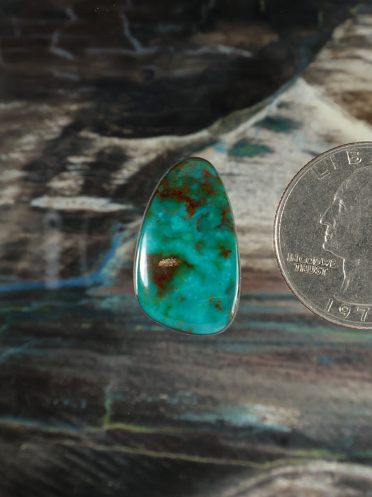 Turquoise teardrop cabochon gemstone with reddish-brown matrix flecks, polished.