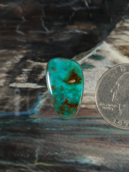 Turquoise teardrop cabochon gemstone with red-brown matrix veining, polished.