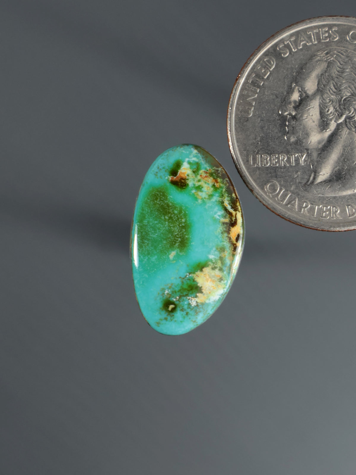 Turquoise oval cabochon gemstone with green and tan speckled inclusions