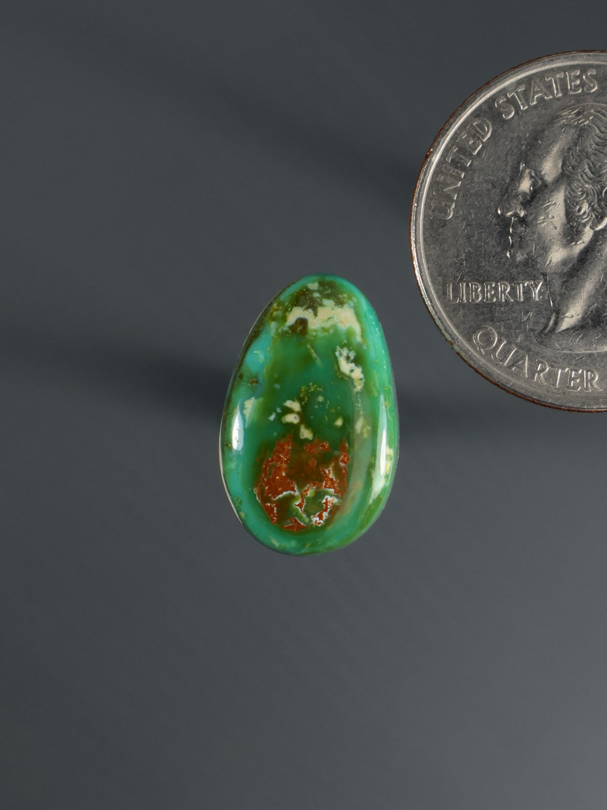 Oval green cabochon gemstone with reddish-brown veining, polished surface