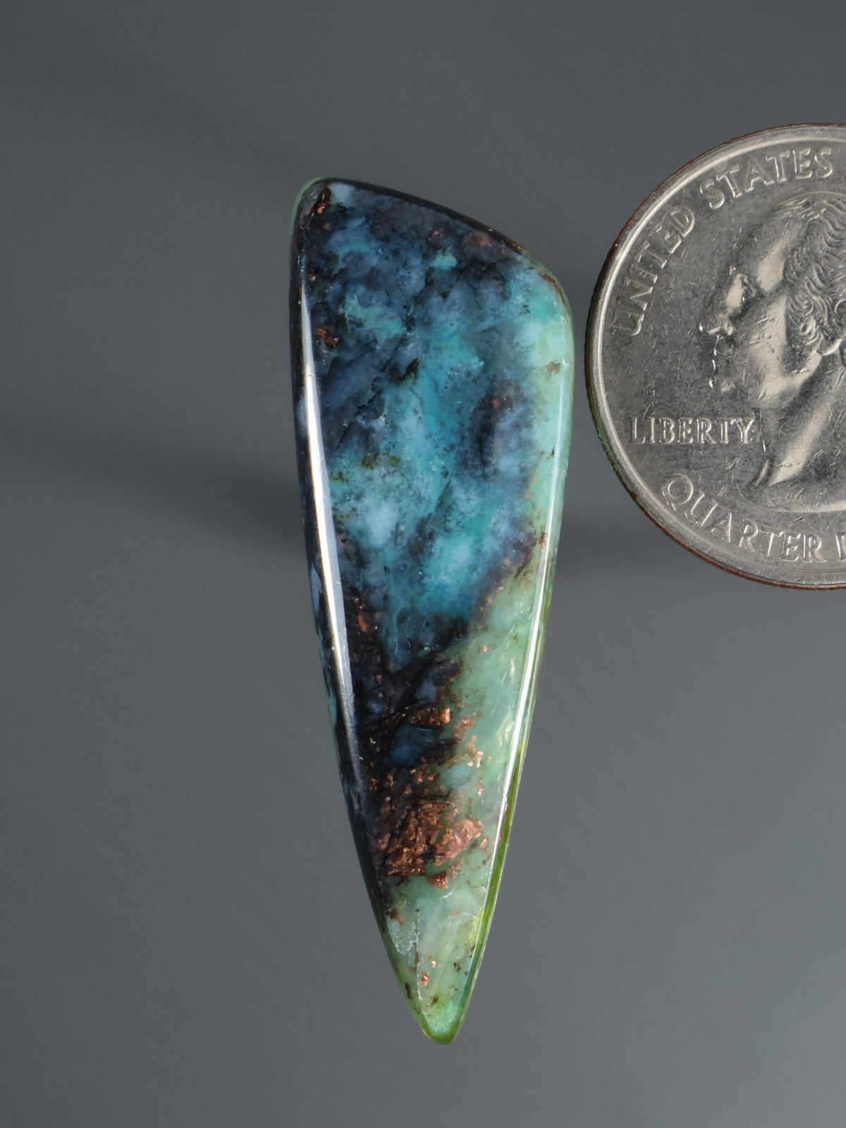 Polished teardrop cabochon gemstone, blue and green with dark matrix.