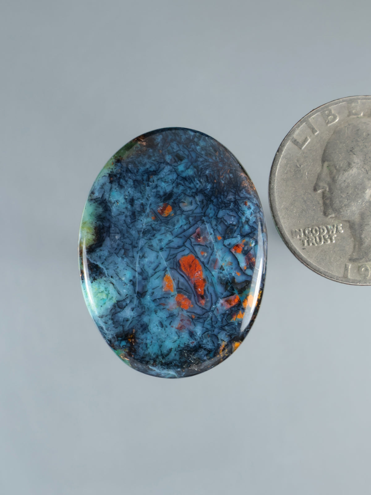 Oval opalized petrified wood cabochon with blue base and orange-red flecks
