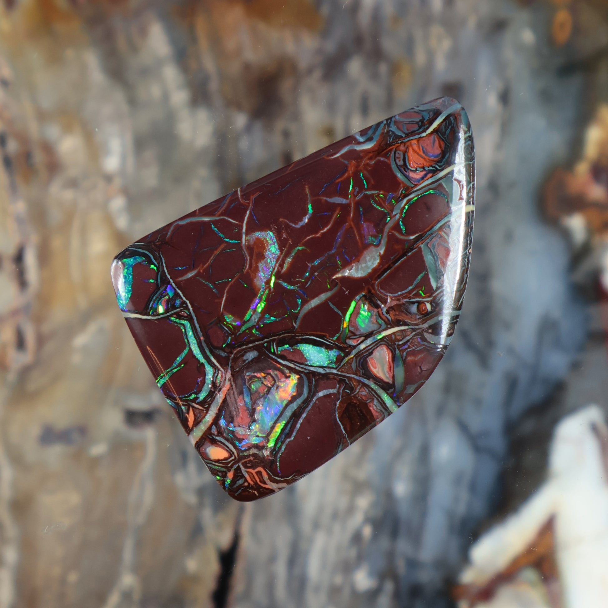 Boulder opal cabochon in marquise shape, burgundy color with vivid green and blue glow