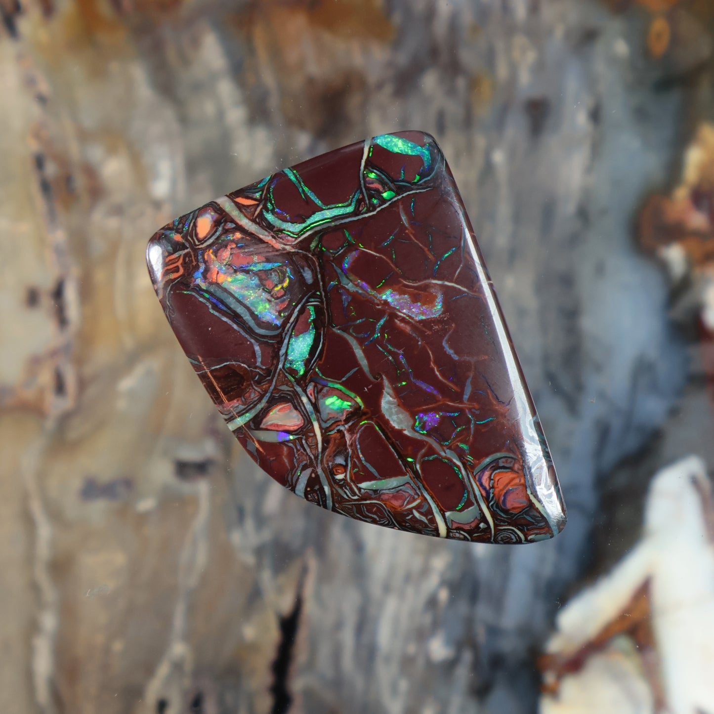 Boulder opal cabochon with maroon-red surface and green highlights, angled long oval shape