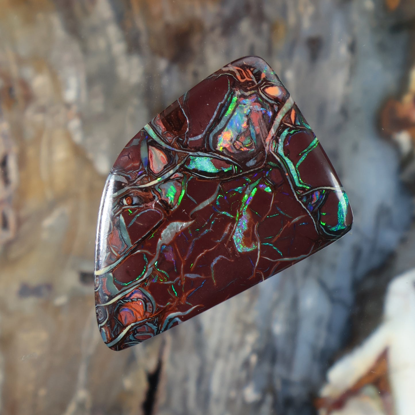 Boulder opal cabochon with dark maroon base, green-blue iridescence, smooth domed top