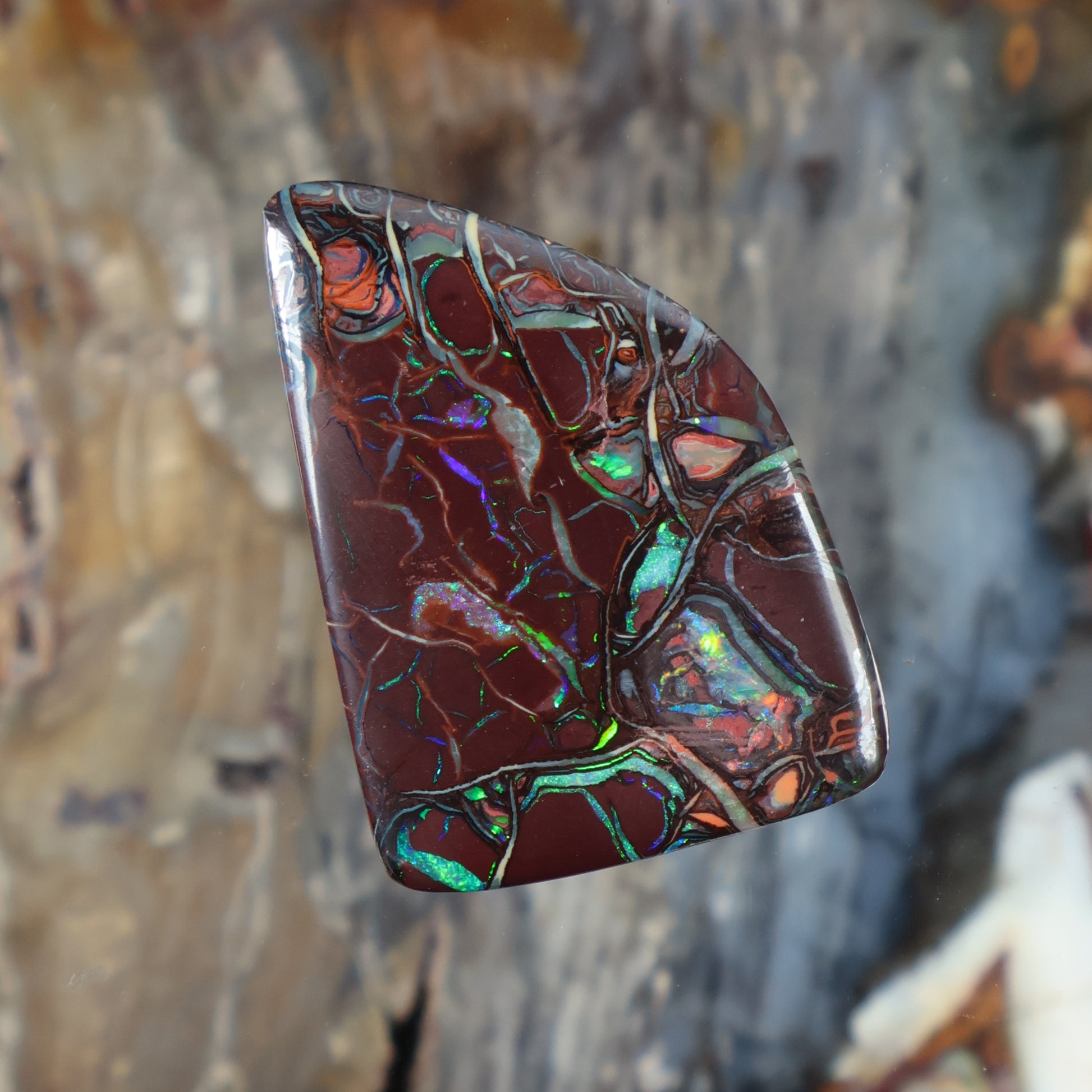 Boulder opal cabochon with maroon body and green-blue iridescent pattern, faceted dome