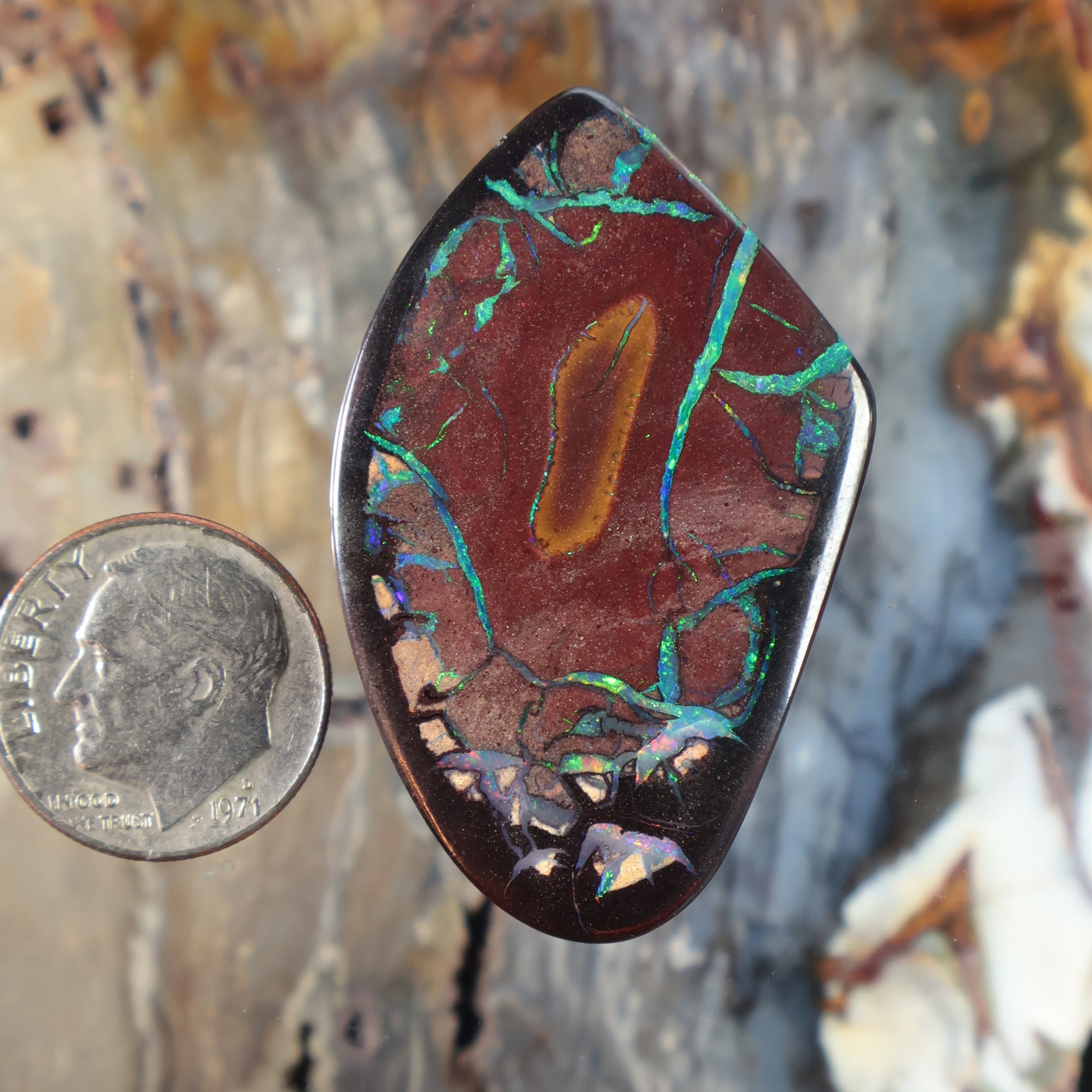 Teardrop boulder opal cabochon with red base and green-blue veining, polished bezel