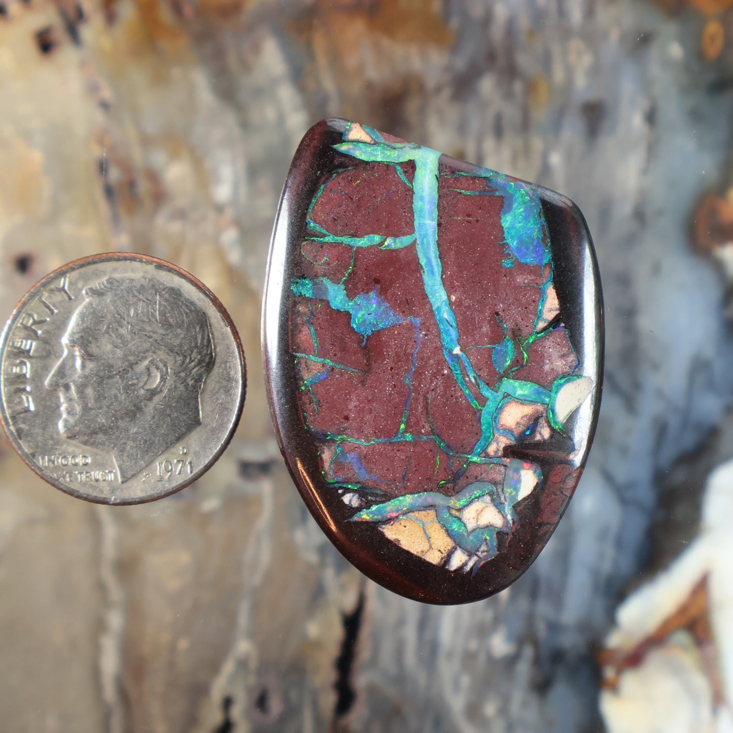 Oval boulder opal cabochon with red stone and teal-blue veining, polished domed face