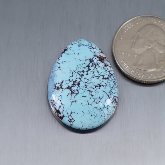 Oval turquoise cabochon with blue surface and red matrix webbing