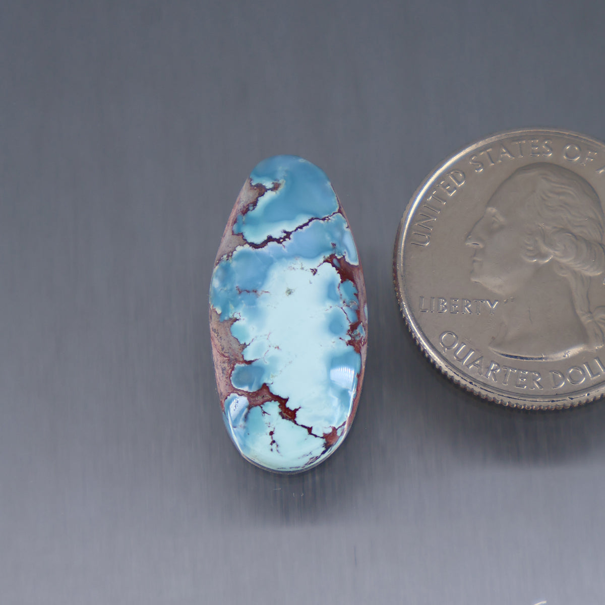 Oval turquoise cabochon gemstone, light blue with red-brown matrix veining
