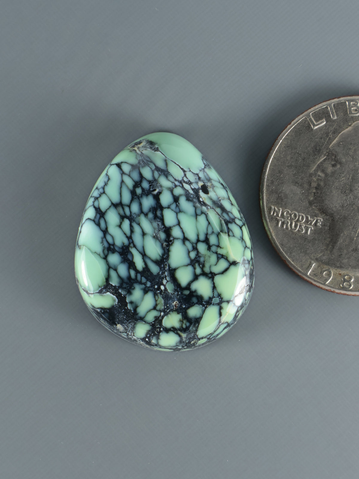 Oval variscite cabochon gemstone, mint green with black webbed matrix pattern.