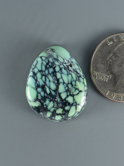 Oval variscite cabochon gemstone, mint green with black webbed matrix pattern.