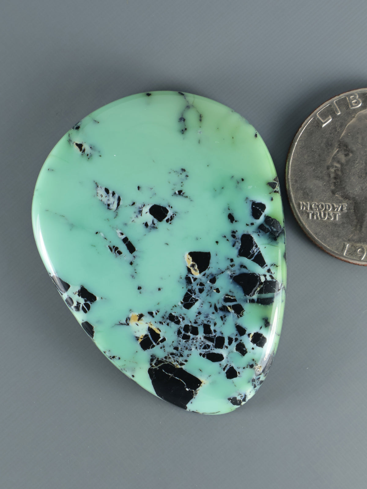 Mint-green variscite cabochon with dark speckled matrix, oval shape
