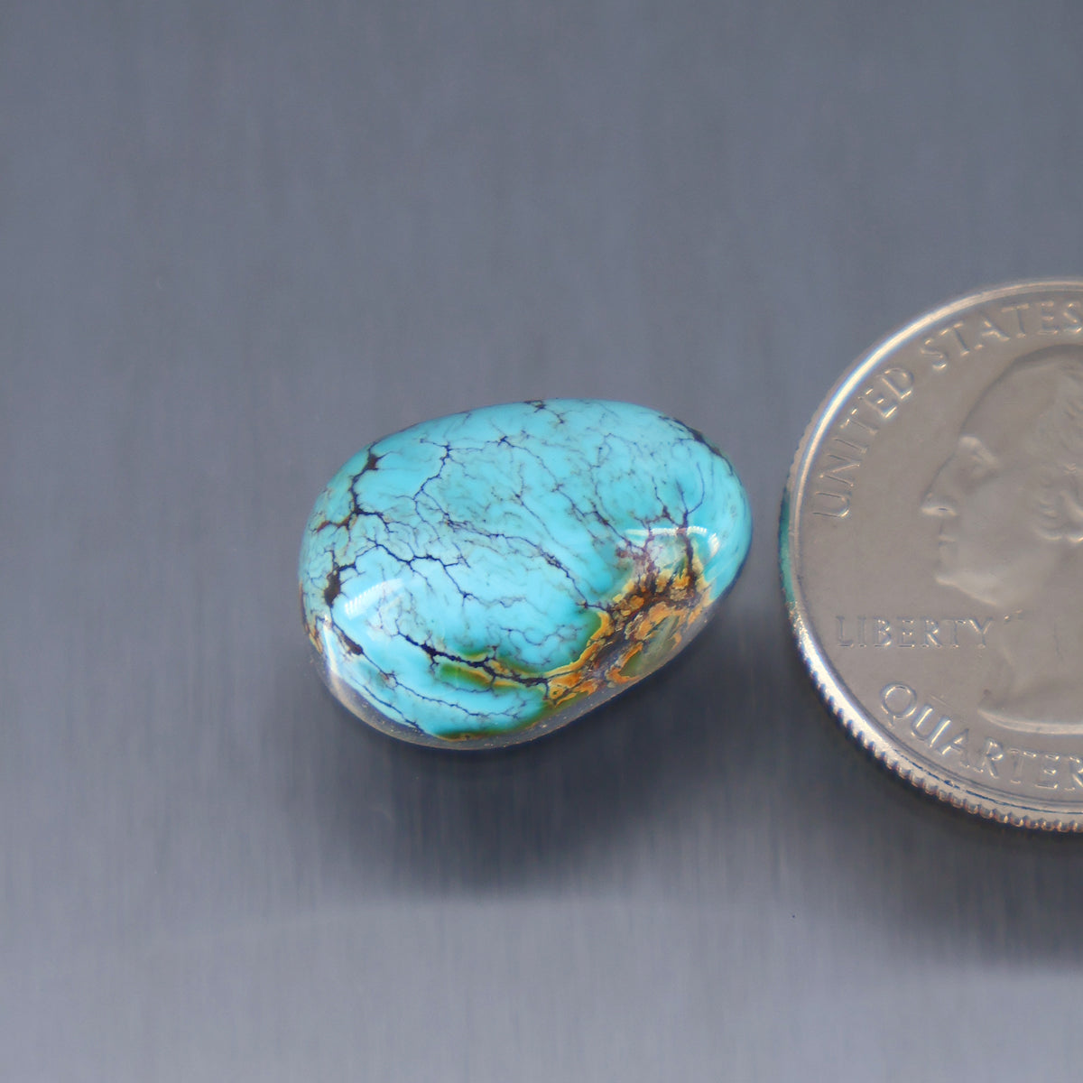 Turquoise cabochon with blue-green color and dark veining, oval shape