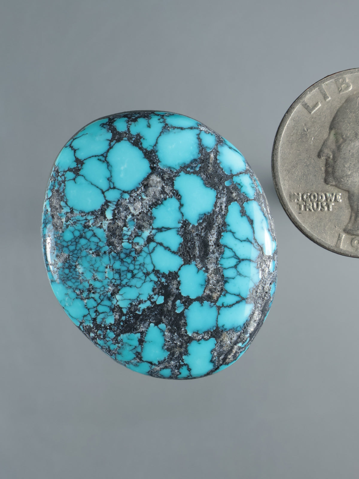 Turquoise cabochon gemstone with black matrix veining and cloud-like patches, oval