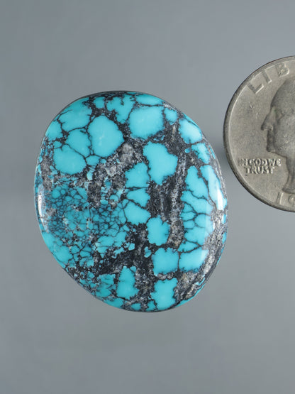 Turquoise cabochon gemstone with black matrix veining and cloud-like patches, oval