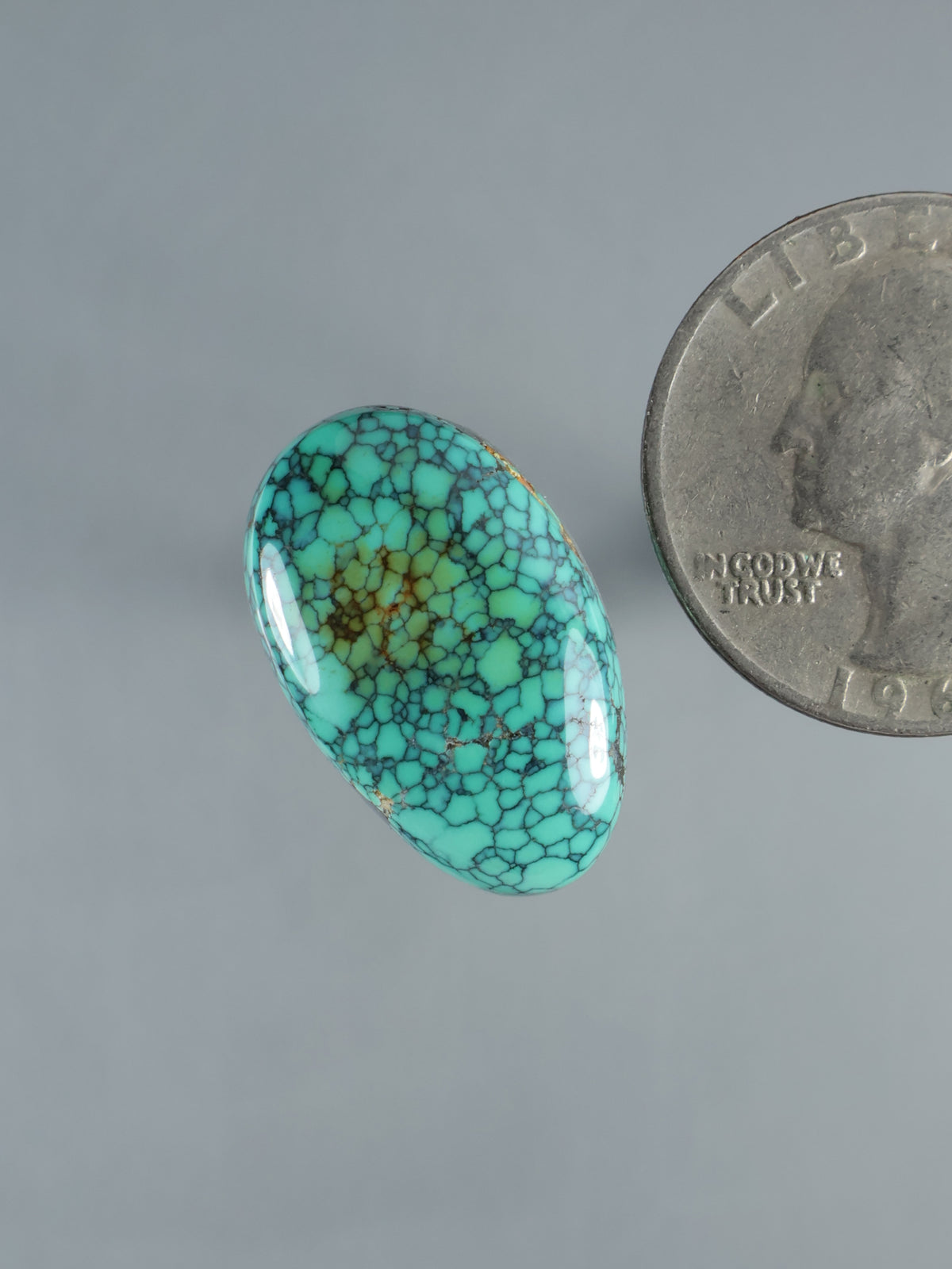 Turquoise oval cabochon gemstone with webbed matrix pattern, angled side view