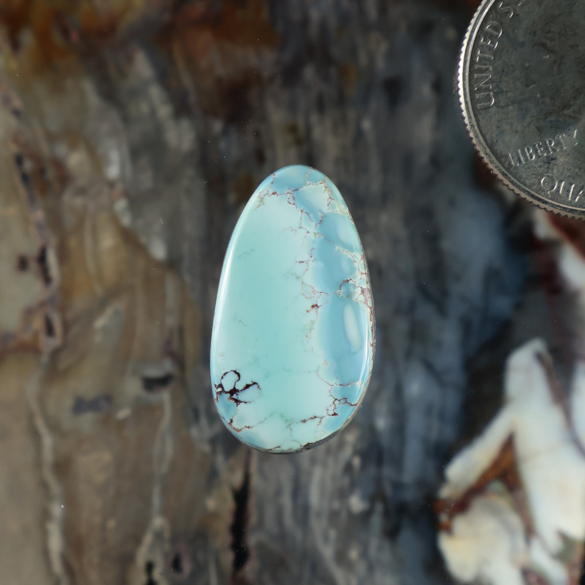 Turquoise oval cabochon with light blue color and thin natural matrix webbing.
