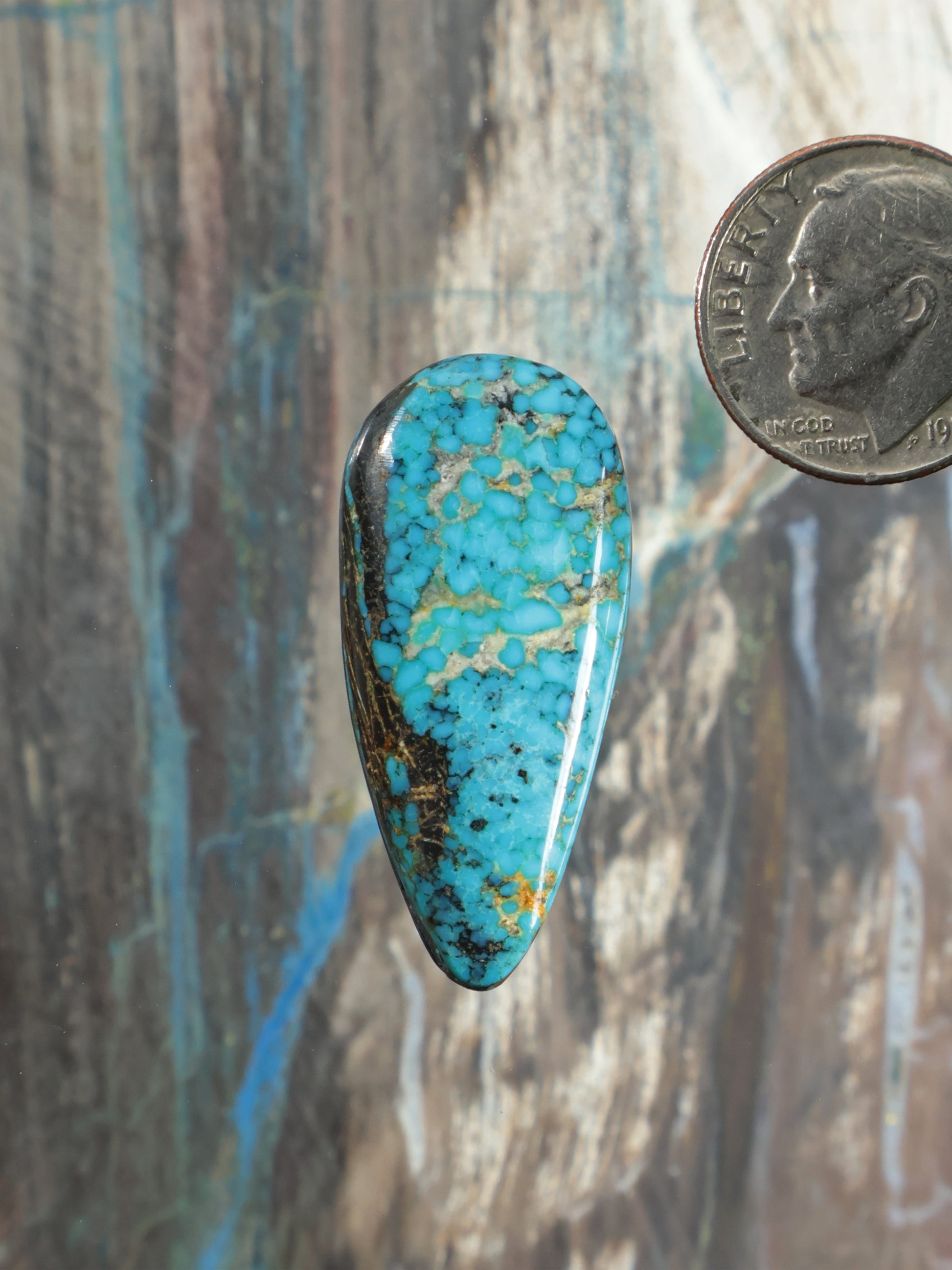 Turquoise cabochon gemstone with teardrop shape, blue and gold veining, set in dark rim