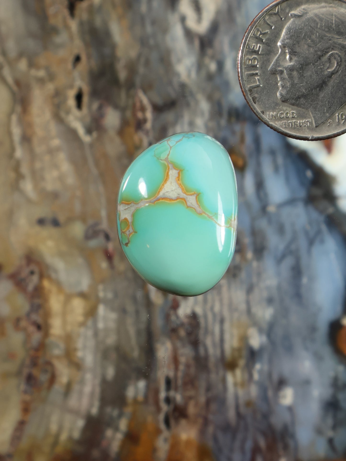 Oval turquoise cabochon gemstone with gold-toned veining, smooth polished surface.