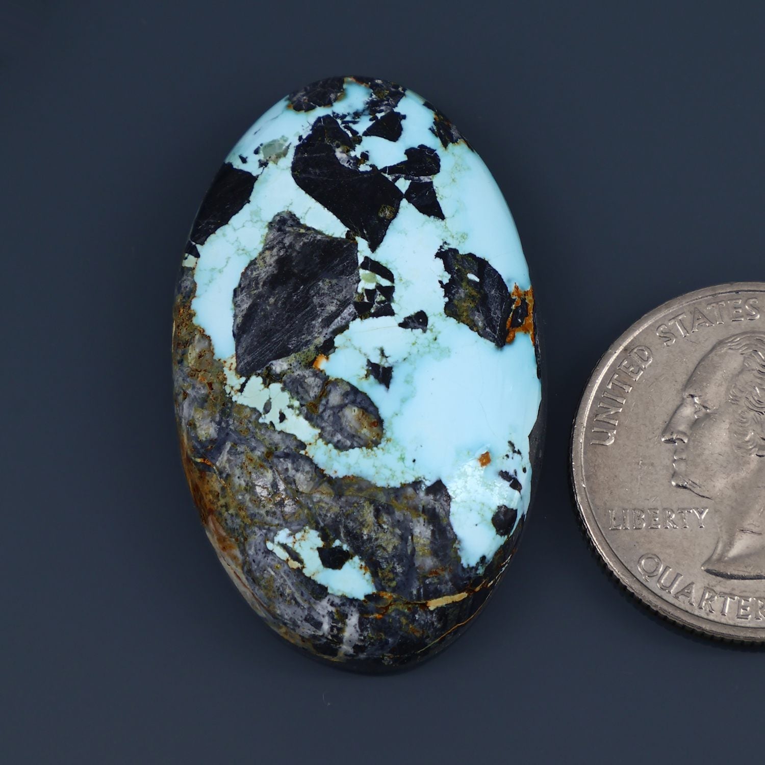 Oval turquoise cabochon with black matrix and gold-brown speckles, polished gemstone