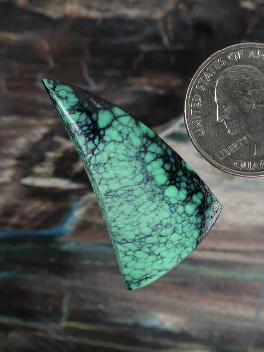 Triangular emerald-green variscite cabochon with dense black veining, polished surface