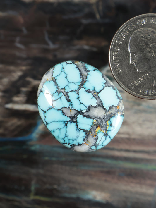 Round turquoise cabochon with blue color and dark webbing, gold flecks
