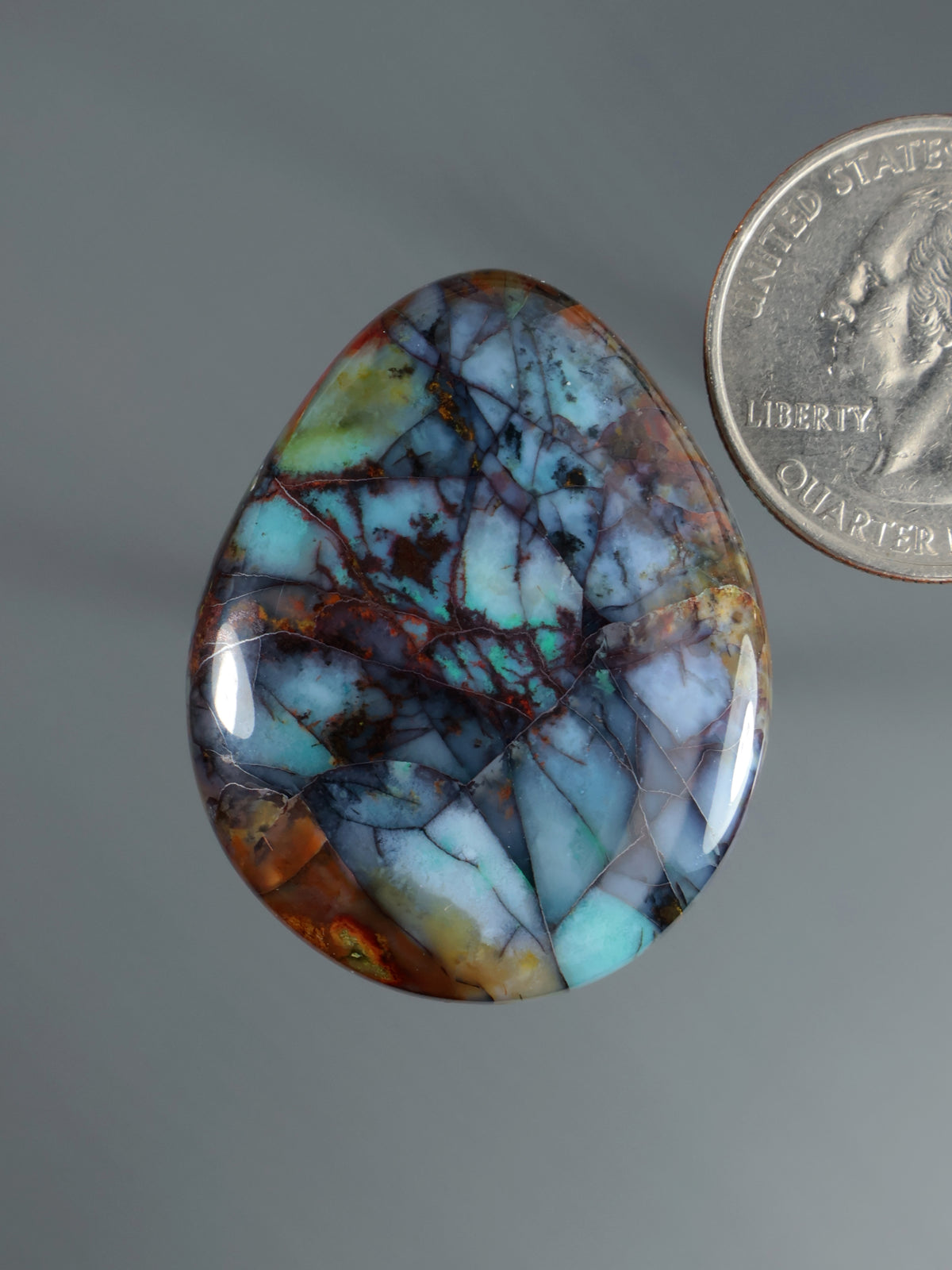 Blue-green teardrop cabochon gemstone with red-brown veining