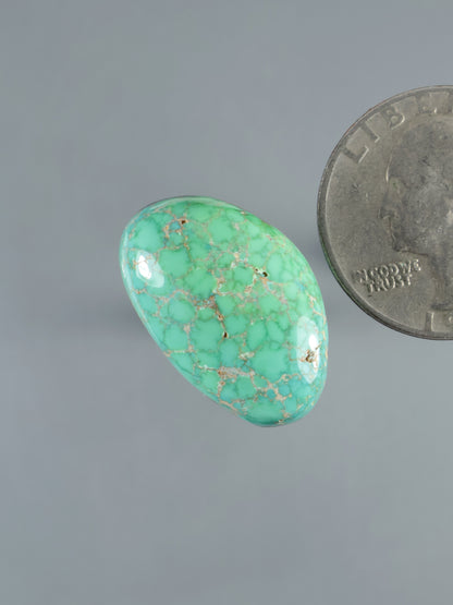 Oval turquoise cabochon gemstone, bright green-blue with webbed matrix veining, polished