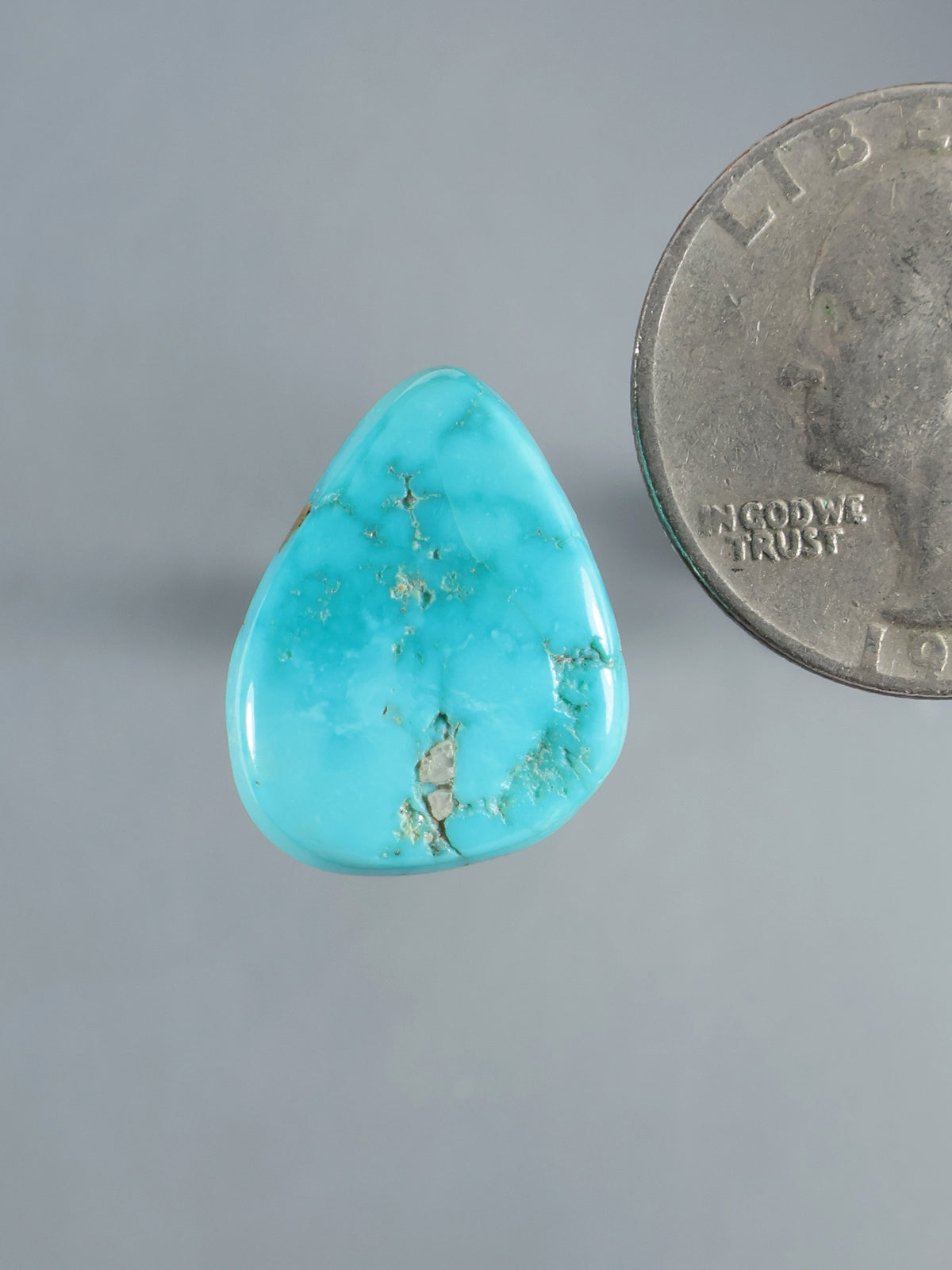 Natural Sleeping Beauty turquoise cabochon, blue-green stone with brown matrix veining beside a coin