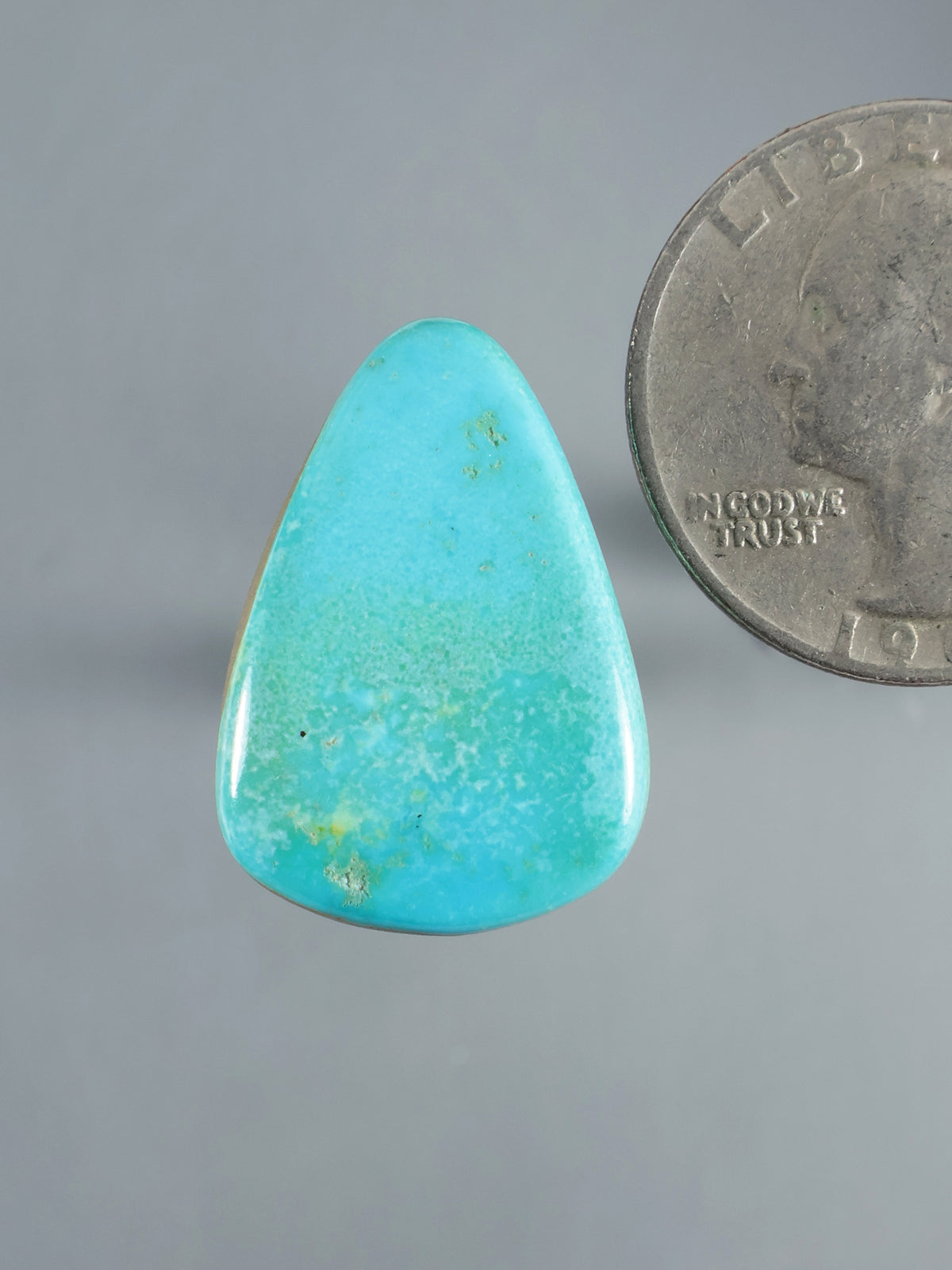 Natural Sleeping Beauty turquoise cabochon, polished blue-green stone shown beside a coin for scale